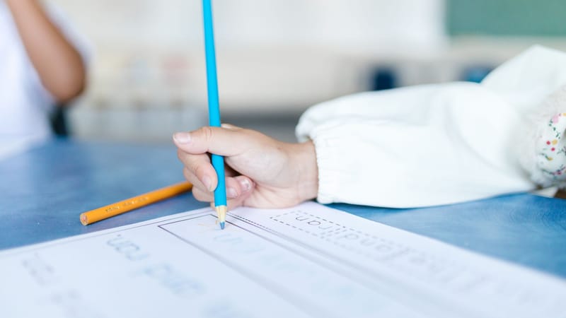 Un enfant écrit sur du papier avec des crayons de couleur, améliorant les compétences motrices fines dans un cadre scolaire.