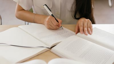 Femme prenant des notes dans un carnet, concentrée sur ses études. Mains visibles en gros plan.