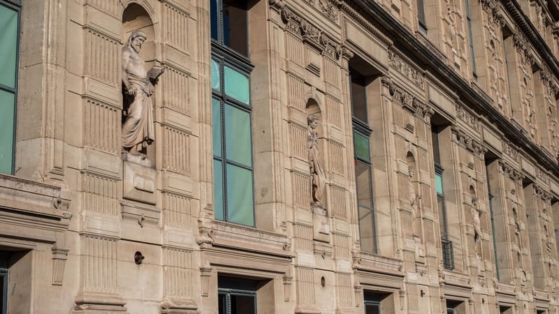 Vue détaillée de la façade historique du musée du Louvre à Paris avec des sculptures.