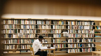 Homme adulte lisant et étudiant dans une bibliothèque bien éclairée avec des étagères de livres.