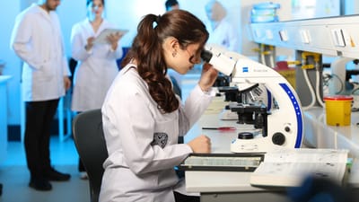 Une jeune scientifique examine des échantillons au microscope dans un laboratoire moderne.