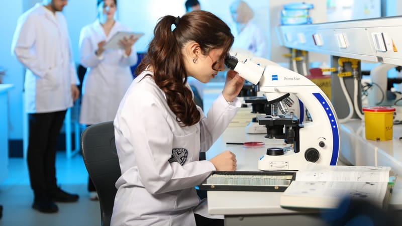 Une jeune scientifique examine des échantillons au microscope dans un laboratoire moderne.