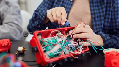 Gros plan sur des mains assemblant un projet robotique avec des fils et des circuits.