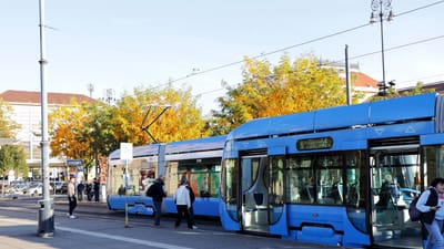 Une scène de rue animée à Zagreb, avec un tramway bleu moderne et des feuillages d'automne.