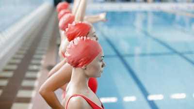 Un groupe concentré de nageuses en bonnets et maillots de bain rouges prêtes pour l'entraînement dans une piscine intérieure.