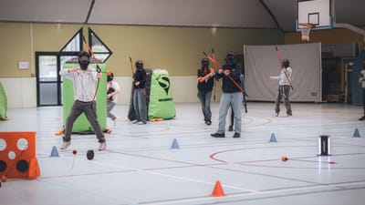 Groupe jouant à l'archery tag à l'intérieur avec des arcs, des flèches et des masques.