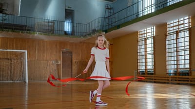 Une jeune fille pratiquant la gymnastique rythmique avec un ruban rouge dans un hall de sport intérieur.