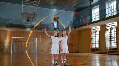 Deux jeunes filles pratiquant la gymnastique rythmique avec des rubans dans un gymnase intérieur.