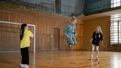 Des enfants s'amusent avec une corde à sauter lors d'une session de jeu dans une salle de sport intérieure.