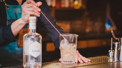 Gros plan sur un barman en train de remuer un cocktail de gin avec des glaçons au comptoir du bar.