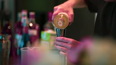 Un barman verse une boisson dans un jigger dans un bar élégant avec des bouteilles en arrière-plan.