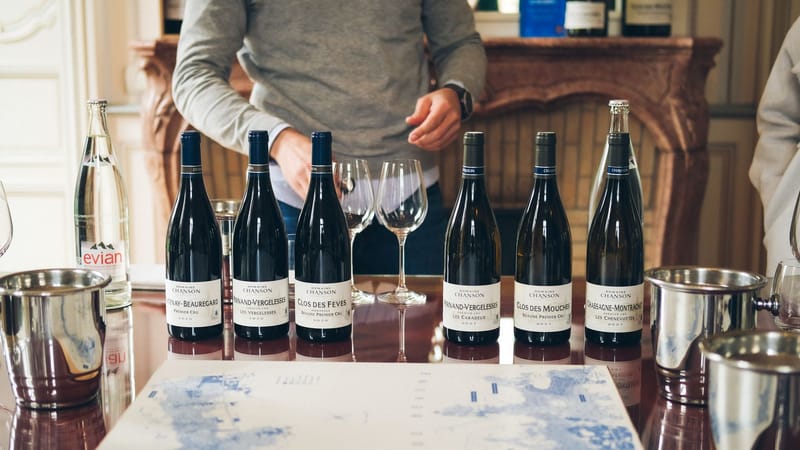 Mise en place d'une table de dégustation de vin avec diverses bouteilles, verres et un sommelier dans un cadre intérieur raffiné.