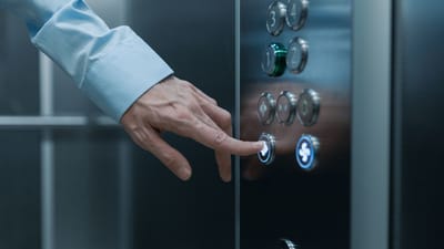 Une personne appuyant sur un bouton d'ascenseur dans un bâtiment moderne, mettant en avant la technologie et la vie urbaine.