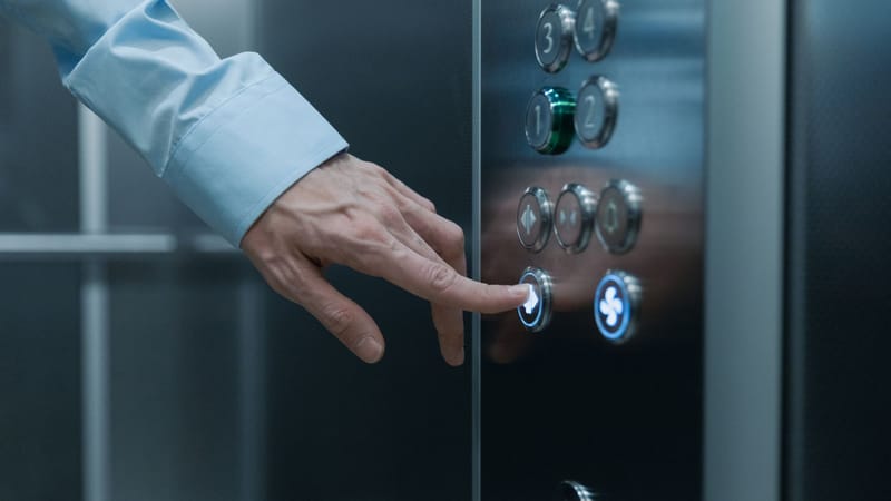 Une personne appuyant sur un bouton d'ascenseur dans un bâtiment moderne, mettant en avant la technologie et la vie urbaine.