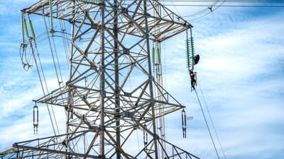 Des travailleurs effectuant l'entretien d'une ligne électrique haute tension sous un ciel bleu.