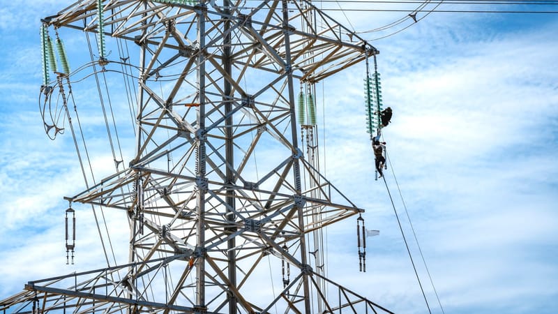 Des travailleurs effectuant l'entretien d'une ligne électrique haute tension sous un ciel bleu.