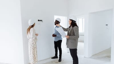 Trois professionnels discutent des plans de design à l'intérieur d'une nouvelle maison portant des casques de sécurité.