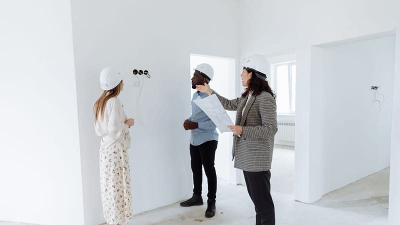 Trois professionnels discutent des plans de design à l'intérieur d'une nouvelle maison portant des casques de sécurité.