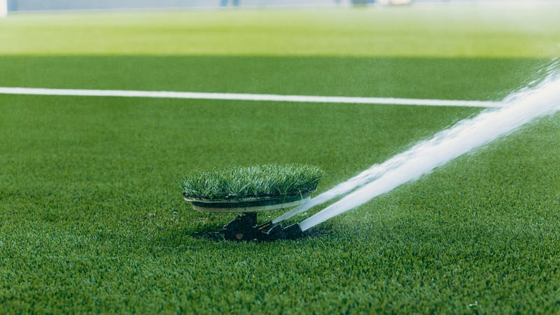 Un arroseur actif arrosant un terrain de sport vert éclatant, mettant en valeur la surface de l'herbe luxuriante.