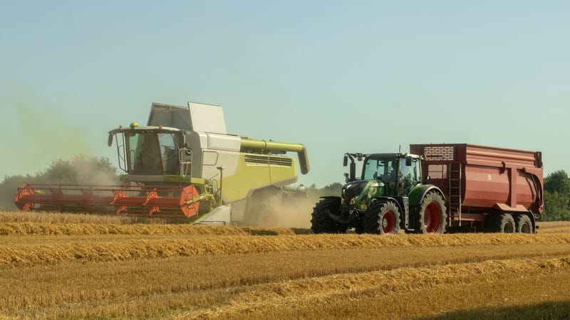 Une moissonneuse-batteuse et un tracteur opèrent dans un champ de blé ensoleillé, capturant l'essence de l'agriculture moderne.