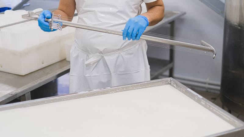 Un travailleur utilisant un outil de fabrication de fromage dans un environnement d'usine, portant des vêtements de protection.