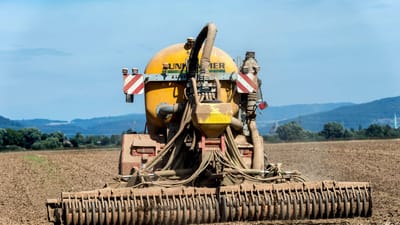 Vue arrière de machines agricoles fertilisant un champ à la campagne sous un ciel bleu clair.