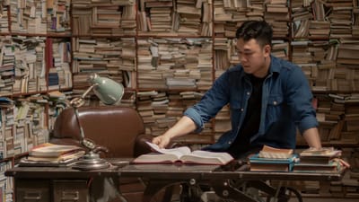 Homme étudiant dans une bibliothèque vintage entourée de livres. Scène de lecture confortable et classique.