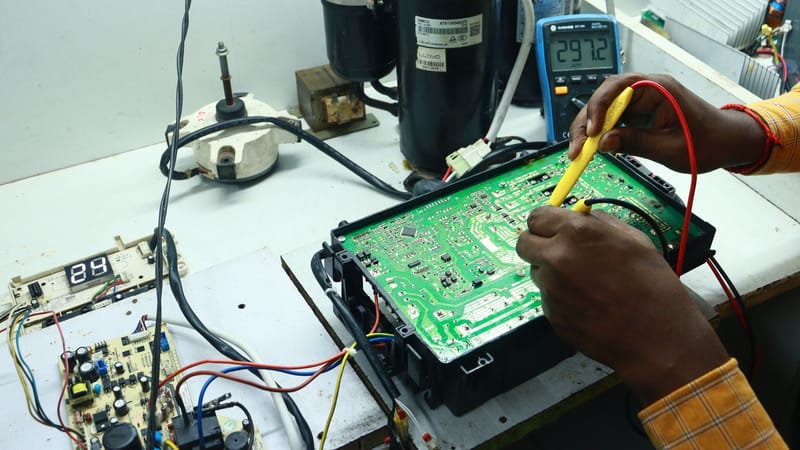 Technicien travaillant sur un PCB AC avec des outils et des équipements, capturé dans un atelier de New Delhi.