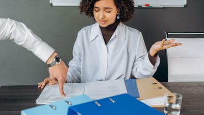 Une femme aux cheveux bouclés est accablée par des papiers dans un bureau, multitâchant avec des documents et des fichiers.