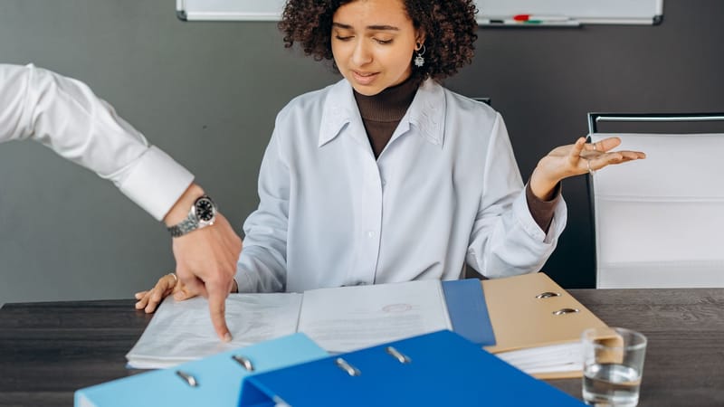 Une femme aux cheveux bouclés est accablée par des papiers dans un bureau, multitâchant avec des documents et des fichiers.