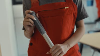Une femme en tablier rouge tenant un manche à balai, en train de nettoyer à l'intérieur.