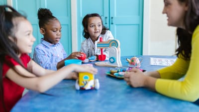 Jeunes enfants jouant avec des jouets et une enseignante dans un environnement préscolaire coloré.