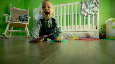 Charmant bébé garçon rampant sur un sol en bois, jouant joyeusement dans une crèche verte vibrante.