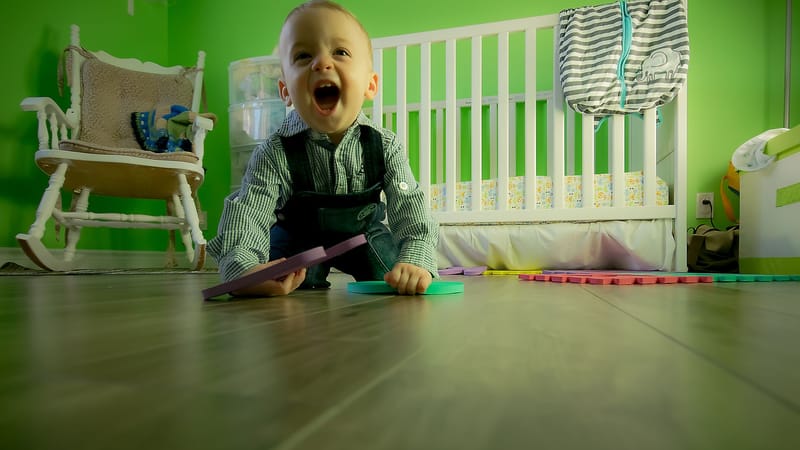 Charmant bébé garçon rampant sur un sol en bois, jouant joyeusement dans une crèche verte vibrante.