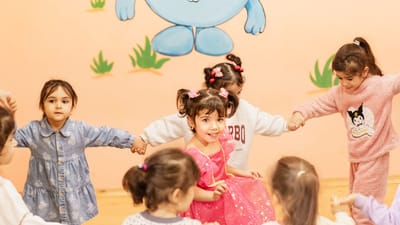 Des enfants joyeux se tiennent la main et participent à un jeu de cercle en intérieur, profitant d'une activité amusante ensemble.