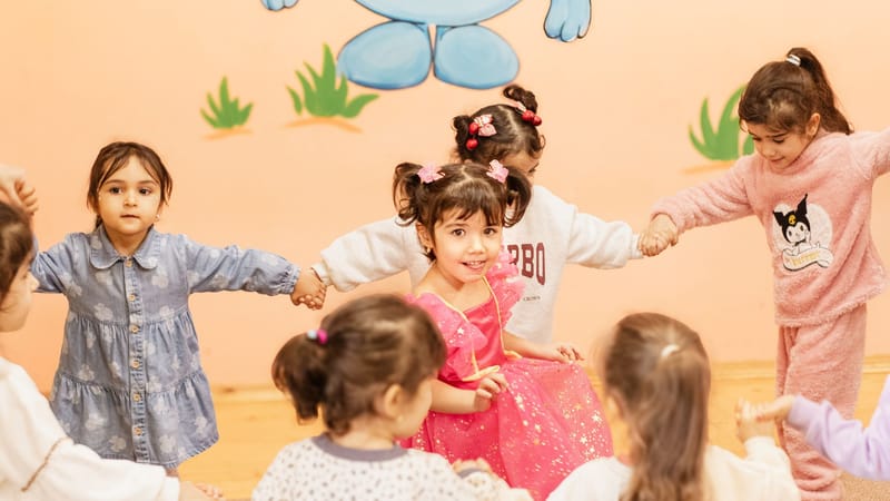 Des enfants joyeux se tiennent la main et participent à un jeu de cercle en intérieur, profitant d'une activité amusante ensemble.