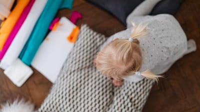 Mignonne petite fille blonde avec des couettes jouant à l'intérieur, entourée de jouets colorés et de coussins.