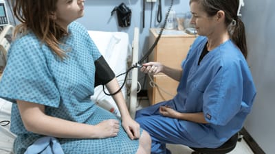 Une infirmière en tenue médicale bleue vérifie la tension artérielle d'une patiente dans une chambre d'hôpital.