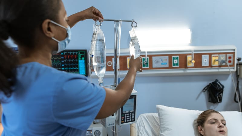 Une infirmière dans un environnement hospitalier ajuste une perfusion pour un patient allongé dans son lit, illustrant les soins médicaux.