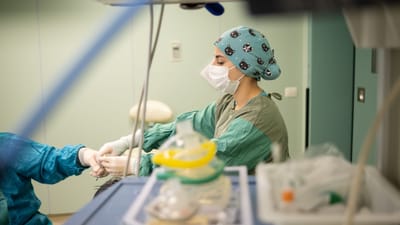 Une infirmière concentrée, portant un masque chirurgical, assiste un chirurgien lors d'une intervention dans une salle d'opération.