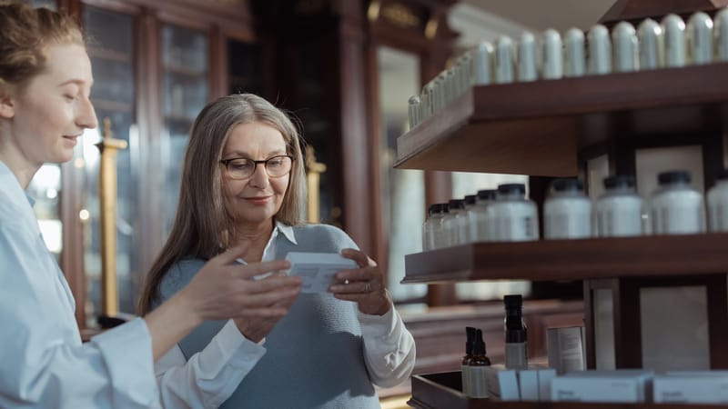 Femme âgée recevant de l'aide d'un pharmacien dans une pharmacie avec des rayons de produits.