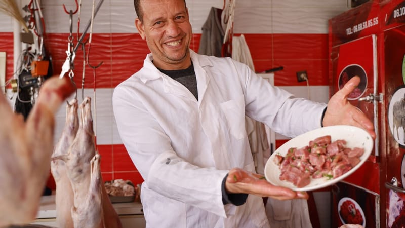 Boucher heureux en manteau blanc présentant une assiette de viande fraîche dans une boucherie colorée.
