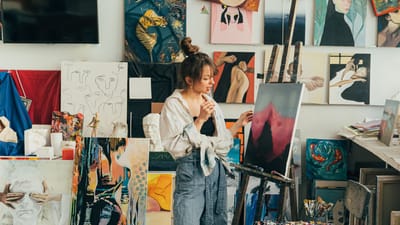 Une artiste femme dans son studio regarde attentivement sa toile parmi une collection de ses œuvres.