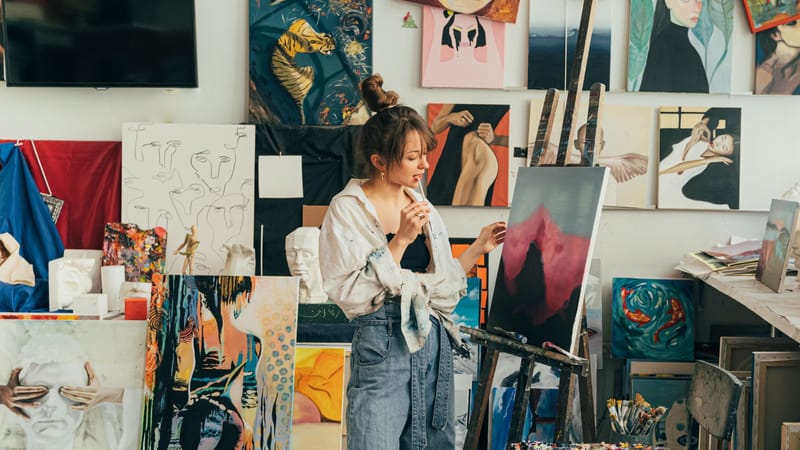Une artiste femme dans son studio regarde attentivement sa toile parmi une collection de ses œuvres.