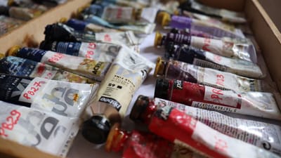 Un gros plan détaillé de divers tubes de peinture dans une boîte en bois, montrant des couleurs vives.