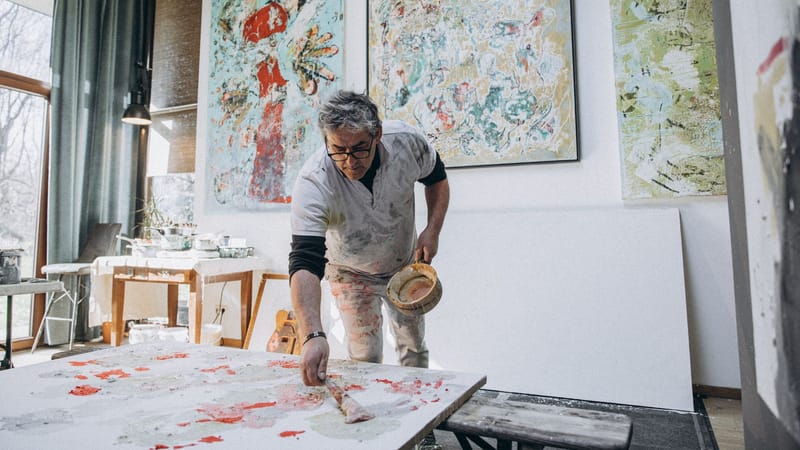 Un peintre masculin talentueux travaillant dans son atelier d'art, entouré de peintures abstraites.