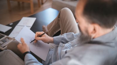 Un homme détendu esquissant sur du papier dans une pièce confortable, montrant créativité et loisirs.