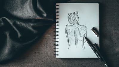 Vue créative de dessus d'un carnet de croquis avec un dessin détaillé d'une figure, des stylos et du tissu.