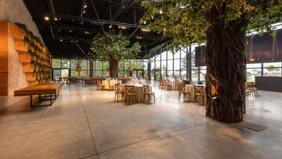 Salle de banquet moderne spacieuse avec des tables élégantes et des arbres d'intérieur luxuriants.