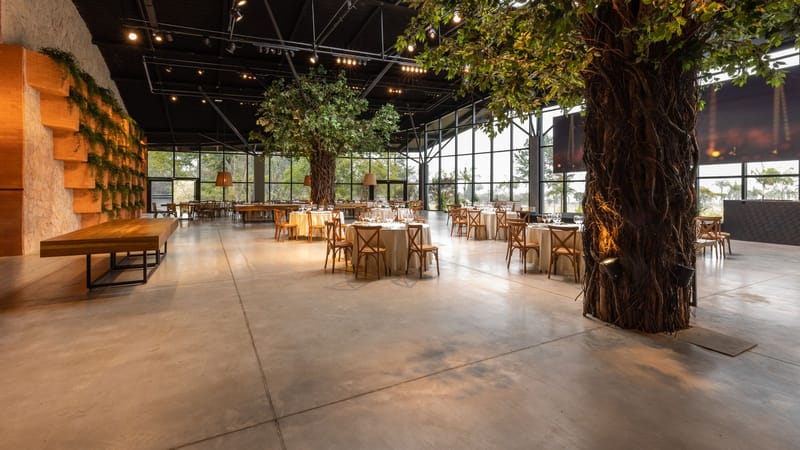 Salle de banquet moderne spacieuse avec des tables élégantes et des arbres d'intérieur luxuriants.